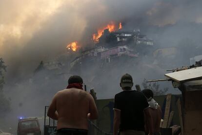 Varias personas miran cómo arden varias viviendas a causa de un incendio forestal que arrasó un sector de la ciudad costera de Valparaíso (Chile) el día de Nochebuena. Dos focos de fuego se generaron de manera simultánea en los cerros de la ciudad situada a unos 100 kilómetros al este de Santiago y avanzaron hasta juntarse y alcanzar su periferia.