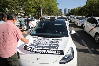 Dos taxistas pegan un cartel de protesta sobre un vehículo en la manifestación en el Paseo de la Castellana, este miércoles.
