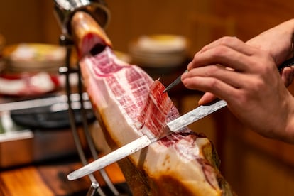 Primer plano de un chef cortando un jamón ibérico, ayudándose de un cuchillo jamonero y una pinza para retirar las lonchas.