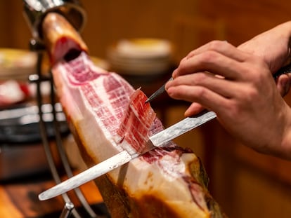 Primer plano de un chef cortando un jamón ibérico, ayudándose de un cuchillo jamonero y una pinza para retirar las lonchas.