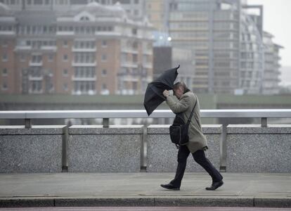 Un hombre se protege del viento y la lluvia mientras camina sobre el London Bridge de Londres.  