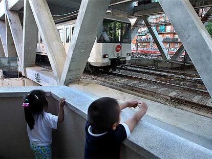 Dos niños desde el balcón de su vivienda de Sants, Barcelona, observan pasar el metro por la estructura del cajón del AVE.
