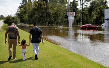 Una pareja camina con su hija después de visitar su casa inundada en Spring Lake, Carolina del Norte.