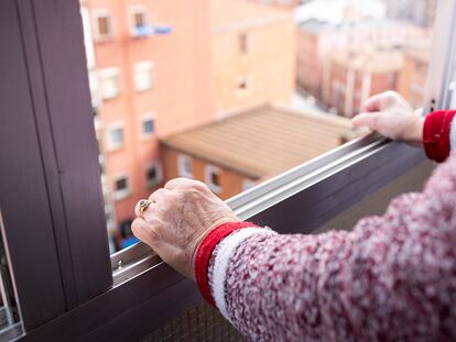 Una anciana se asoma por la ventana de un piso alto en la ciudad.