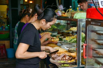 El periodo colonial francés dejó en <a href="https://elviajero.elpais.com/tag/vietnam/a" rel="nofollow" target="_blank">Vietnam</a> una preparación tradicional servida entre 'baguettes' de plan blanco que primero fueron de trigo y después de harina de arroz: el 'banh mi'. Presenta una gran variedad de sabores y texturas, está rico y es barato, por lo que se ha convertido en un bocado muy extendido en el país asiático, donde se vende en puestos callejeros. Tiene, como ingredientes más populares, carne, paté (otro recordatorio de su herencia francesa), chicharros; zanahoria, 'daikon' (rábano de invierno de sabor suave) u otras verduras encurtidas; chile, pepino y cilantro. Las rebanadas se untan con mayonesa. En la imagen, un puesto de un mercado en la ciudad vietnamita de Hoi An donde preparan este plato tradicional.