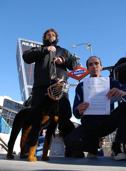 Dos voluntarios de la asociación posan con la denuncia y el perro de peluche que usan en la campaña.