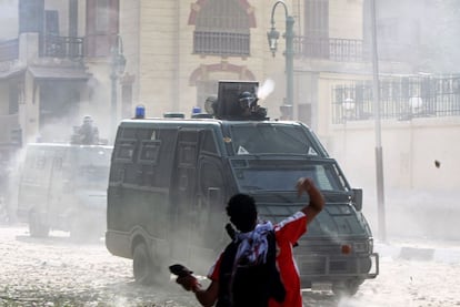 Un manifestante lanza piedras contra una furgoneta policial, mientras un agente dispara un artefacto de bombas lacrimógenas.