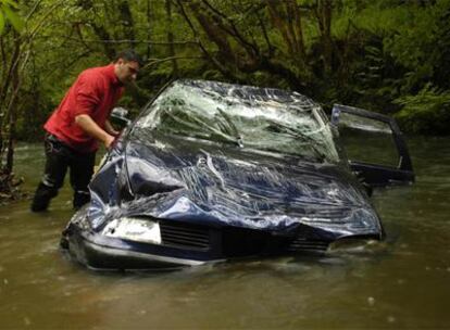 Un hombre revisa el interior del coche tras ser izado del agua y rescatados los cadáveres y la única superviviente.