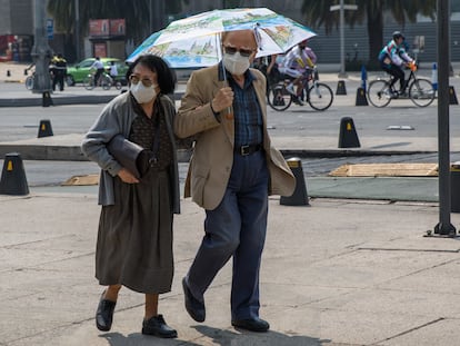 Una pareja de la tercera edad camina sobre Paseo de la Reforma protegiéndose de los rayos del sol con un paraguas, en Ciudad de México.