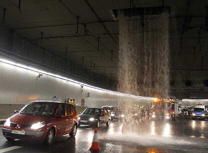 Una gran cascada de agua, en el centro de la imagen, cae sobre el túnel de la M-30 de Madrid mientras los vehículos circulan a su lado.