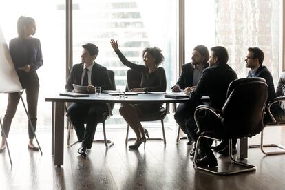 Smiling black businesswoman raising hand asking female lead in boardroom - Estar donde estés - Banco Sabadell - Tipos de personalidades en las reuniones