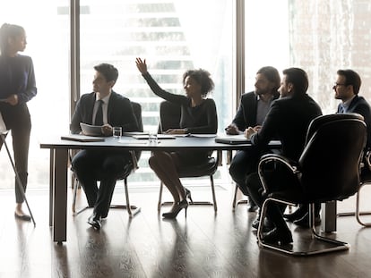 Smiling black businesswoman raising hand asking female lead in boardroom - Estar donde estés - Banco Sabadell - Tipos de personalidades en las reuniones