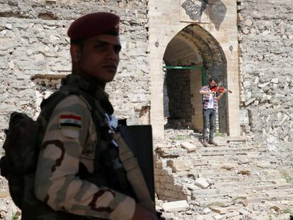 Un militar hace guardia en unas ruinas en Mosul. De fondo, un violinista que vivi&oacute; bajo el r&eacute;gimen del ISIS toca una pieza.