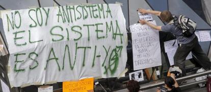 Uno de los jóvenes acampados en la Puerta del Sol de Madrid que permanecen en el 'kilómetro cero' de España desde que el domingo coloca unas pancartas.