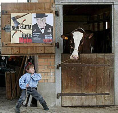 Un niño suizo juega con una vaca junto a carteles que piden el <i>no</i> a la ONU.