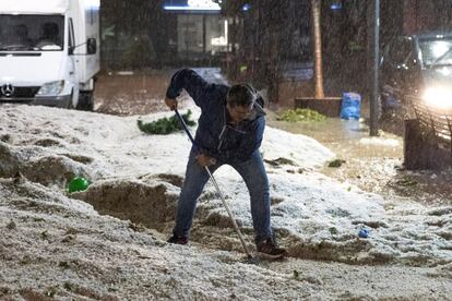 Una persona trabaja para hacer un camino entre el granizo caido esta tarde en Arganda del Rey, para poder cruzar una.