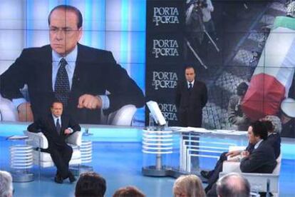 El primer ministro italiano, izquierda, responde a las preguntas de los periodistas de la RAI con la imágenes de fondo del funeral del agente Nicola Calipari.