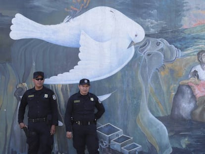 Policiais salvadorenhos diante de um mural que faz alusão à guerra civil de El Salvador (1980-92).