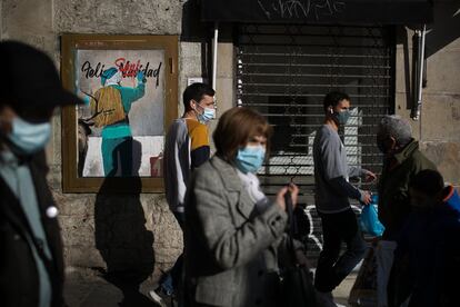 Varias personas pasan por delante de una pintada en la que se puede ver un Papa Noel con el lema "Feliz Sanidad", obra el artista callejero TVBOY, en una calle de Barcelona. En Cataluña, bares y restaurantes pueden abrir en dos franjas horarias: de 7.30 a 9.30, para servir desayunos, y de 13.00 a 15.30, para comidas. Los establecimientos con comida para llevar podrán hacerlo hasta las diez de la noche. El servicio a domicilio se mantiene hasta las 23.00. El interior de los locales solo podrá ocuparse con un aforo del 30%.