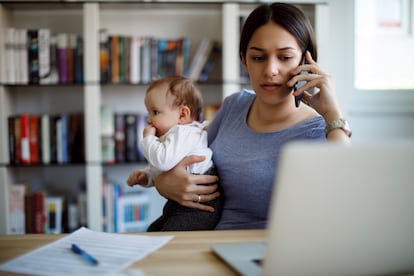 Una mujer teletrabaja con su bebé en brazos.