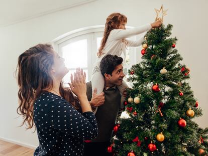 Family decorating a Christmas tree. Young man with his daughter on his shoulders helping her to place a star on Christmas tree.