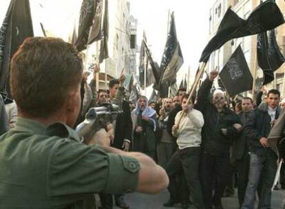 Un policía palestino apunta con su arma a los manifestantes durante una protesta contra la cumbre de Annapolis ayer en Hebrón.