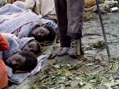 Los victoriosos tutsis del FPR formaron un Gobierno en Kigali e instaron a los refugiados a regresar al país, pero al mismo tiempo pidieron a la comunidad internacional la formación de un tribunal para juzgar a los hutus por genocidio. En la imagen, tres refugiados tutsis se acurrucan para protegerse del frío y la humedad mientras pasa junto a ellos un hombre con la pierna amputada, en un campamento al sur de Ruanda, el 20 de mayo de 1994.