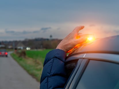 Una persona poniendo la baliza v16 en el techo de su coche durante un viaje en carretera.