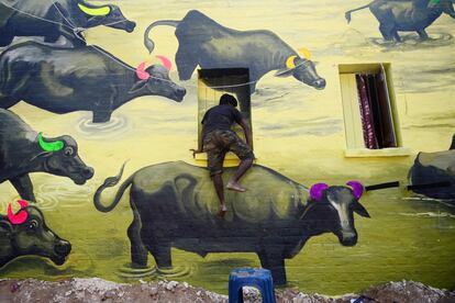 Un artista indio se sube a una ventana mientras trabaja en un mural de búfalos en una pared en Railway Colony, creado como parte del proyecto 'Paint My City' para el próximo festival Kumbh Mela, en Allahabad. 