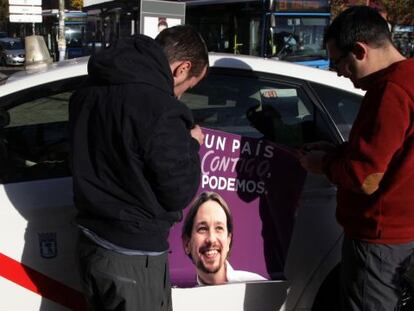 Dos taxista colocan publicidad electoral de Podemos en 2015.