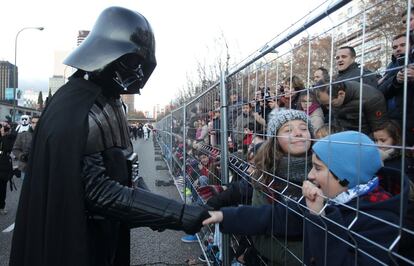 Dos niños saludan a un hombre disfrazado de Darth Vader antes de iniciarse el desfile de la cabalgata en Madrid.