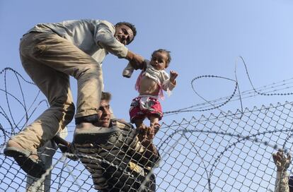 Un niño sirio es alzado sobre las cercas fronterizas para entrar en territorio turco.