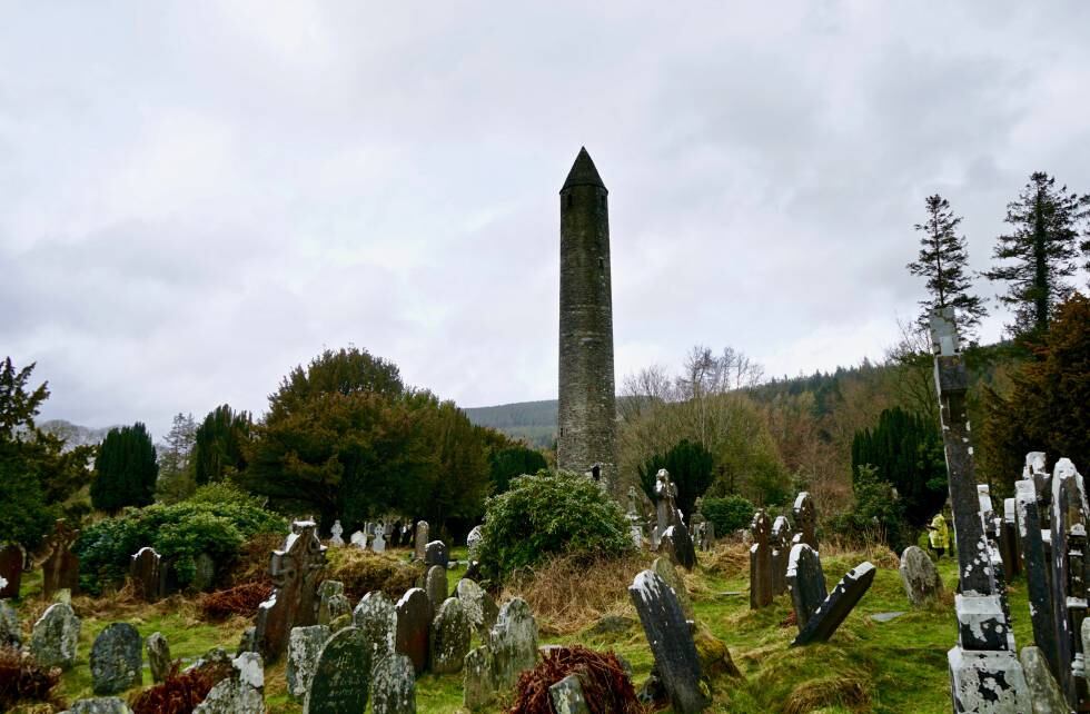 La torre cilíndrica de las ruinas de Glendalough entre lápidas y cruces celtas.