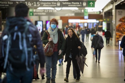 Una mujer sin mascarilla camina entre viajeros con cubrebocas en la estación de Atocha, este miércoles. La nueva normativa del Ministerio de Sanidad da la potestad a la empresa de decidir si sus trabajadores deben seguir usándolas en espacios interiores.