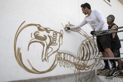 En la imagen, Nychos dibuja con espray un esqueleto cerca del suelo en una de las paredes del silo.