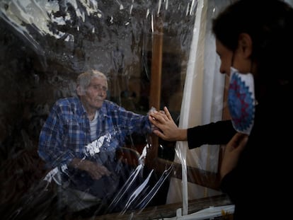 Víctor Tripiana extiende la mano para tocar la mano de su familiar a través de una lámina de plástico en la residencia de ancianos Reminiscencias en Tandil, Argentina, el 4 de abril.