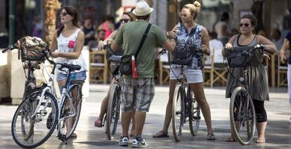 Cuatro turistas en bicicleta escuchan las indicaciones de su guía en el centro histórico de Valencia.
