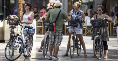 Cuatro turistas en bicicleta escuchan las indicaciones de su gu&iacute;a en el centro hist&oacute;rico de Valencia. 