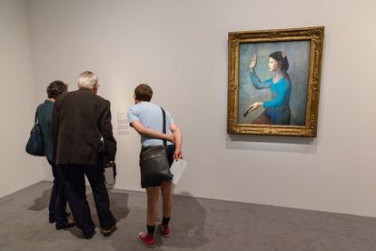 Tres personas leen la información de una de las obras expuestas en la exposición.