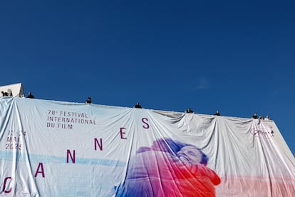 Colocación de la lona con el cartel del festival, una imagen de 'Un hombre y una mujer', de Claude Lelouch, con Anouk Aimée y Jean-Louis Trintignant, en una de las fachadas del Palacio de festivales.

