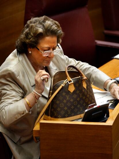 Rita Barberá busca algo en su bolso que lleva estampada la marca Louis Vuitton en un pleno de las Cortes