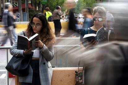 Dos mujeres leen los libros de Alice Kellen mientras hacen cola para que la autora les firme el ejemplar, este domingo en Sant Jordi.