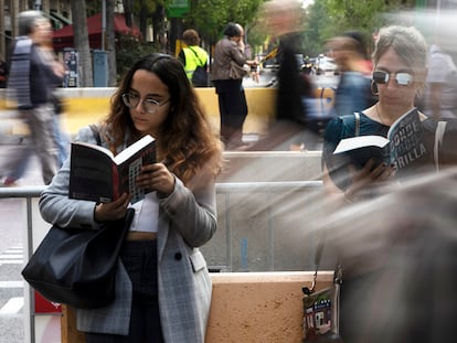 Dos mujeres leen los libros de Alice Kellen mientras hacen cola para que la autora les firme el ejemplar, este domingo en Sant Jordi.