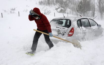Una mujer intenta sacar su coche de la nieve en el municipio de Los Barrios de Luna, en León.