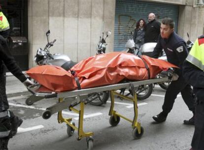 Dos operarios retiran el cadáver de uno de los fallecidos en un edificio de la calle Escipión de Barcelona.