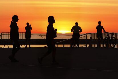 Varias personas pasean y hacen deporte al amanecer en la playa de la Nova Icària de Barcelona este jueves.