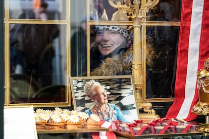 A woman wearing a crown smiles behind a window of a cafe where a picture of Danish Queen Margrethe is on display in Copenhagen, Denmark, Sunday, Jan. 14, 2024.