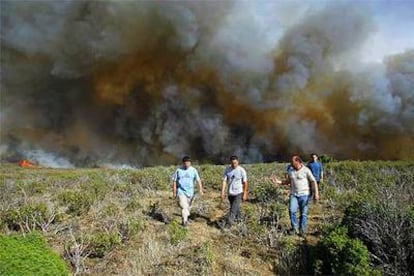 Varios hombres se alejan del fuego en la localidad guadalajareña de Santa María del Espino.