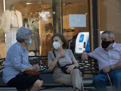 Jubilados ataviados con mascarillas conversan en un banco.