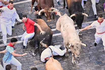 Varios corredores caen al suelo al paso de los astados de la ganadería de Álvaro Núñez, durante el tercer encierro por las calles de Pamplona.